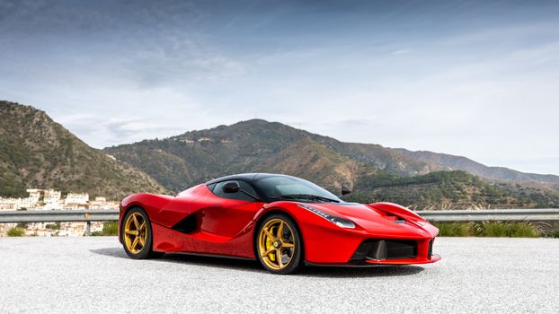 Sleek red sports car parked on a mountain road with a stunning backdrop.
