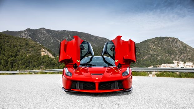 Striking red sports car with gullwing doors open on a scenic mountain road.