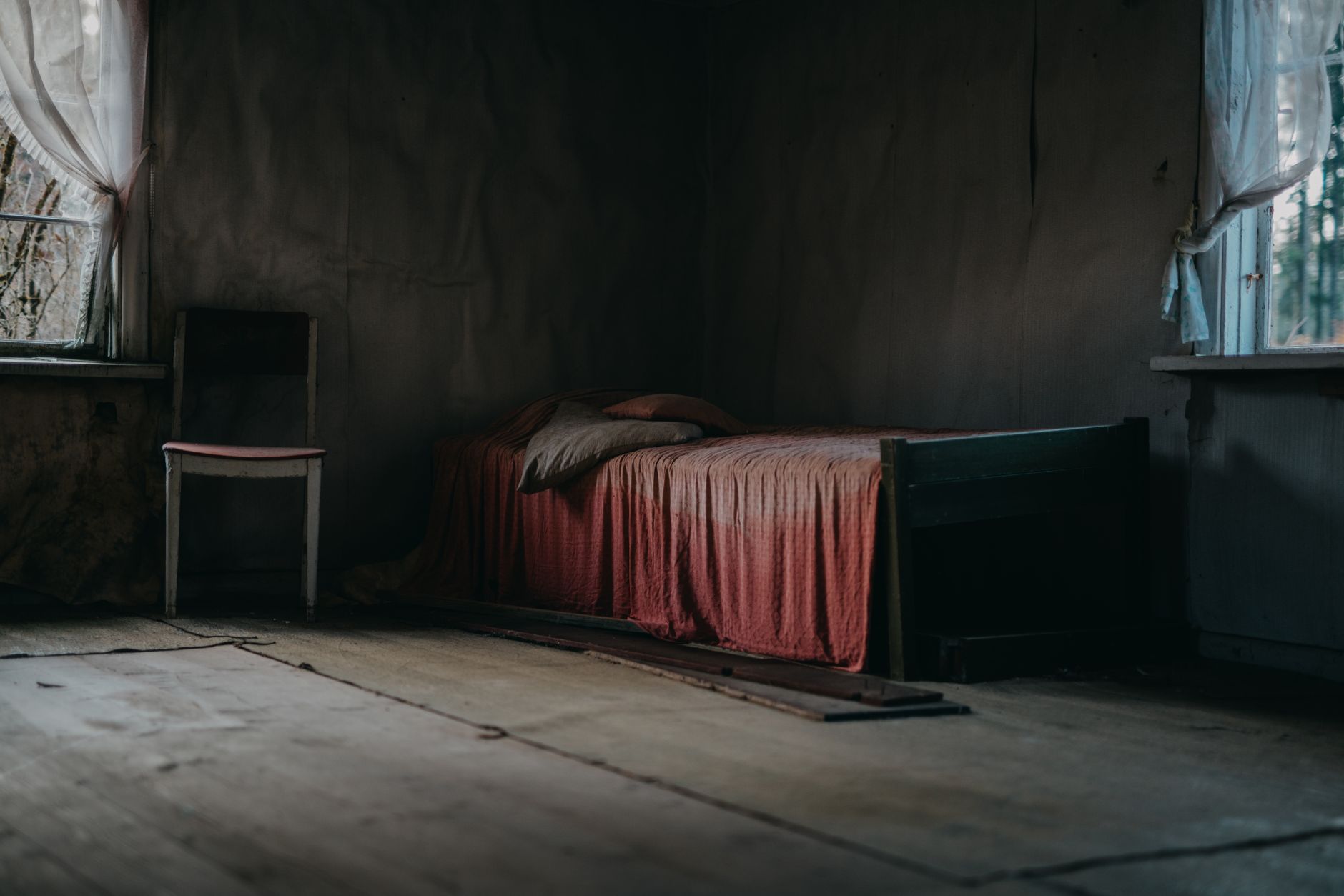 臥室怎麼整理才不積灰?減少布面與死角實用法 Moody, textured room with an old bed and wooden chair showcasing abandonment.