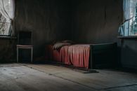房间里有一张旧床和一把木椅，喜怒无常且纹理丰富，尽显遗弃之感
