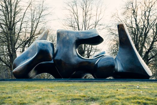 Large abstract bronze sculpture surrounded by leafless trees in a park setting.