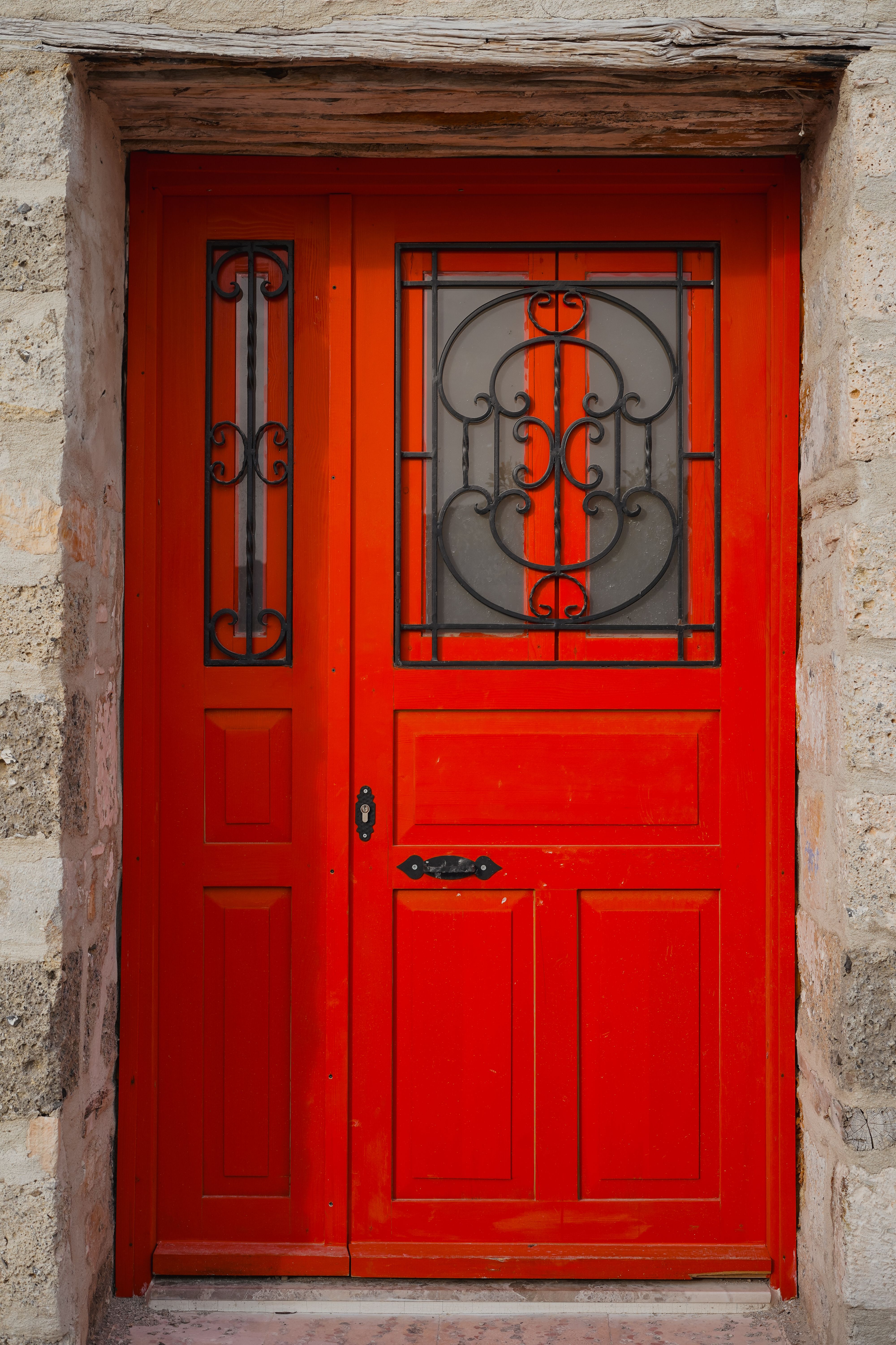 A striking red door featuring intricate iron grillwork set in a stone wall.