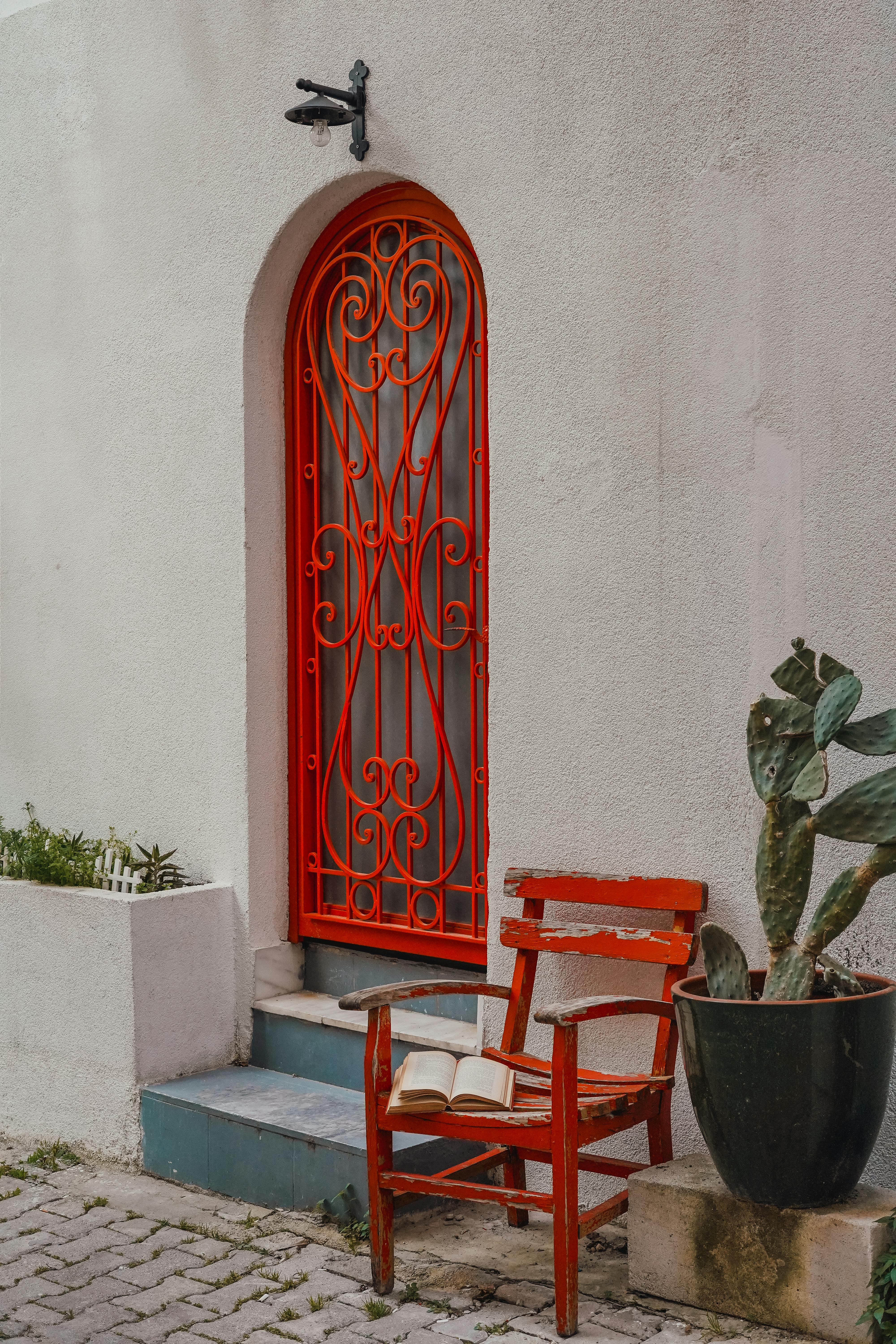 Stylish red arched door with ornate design beside a rustic chair.
