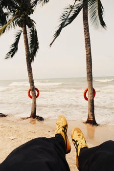 Person relaxing by the beach with palm trees and ocean waves in view.