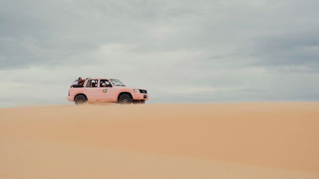 A pink SUV navigating through desert sands under an overcast sky, perfect for adventure themes.