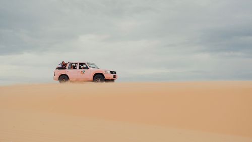Free A pink SUV navigating through desert sands under an overcast sky, perfect for adventure themes. Stock Photo