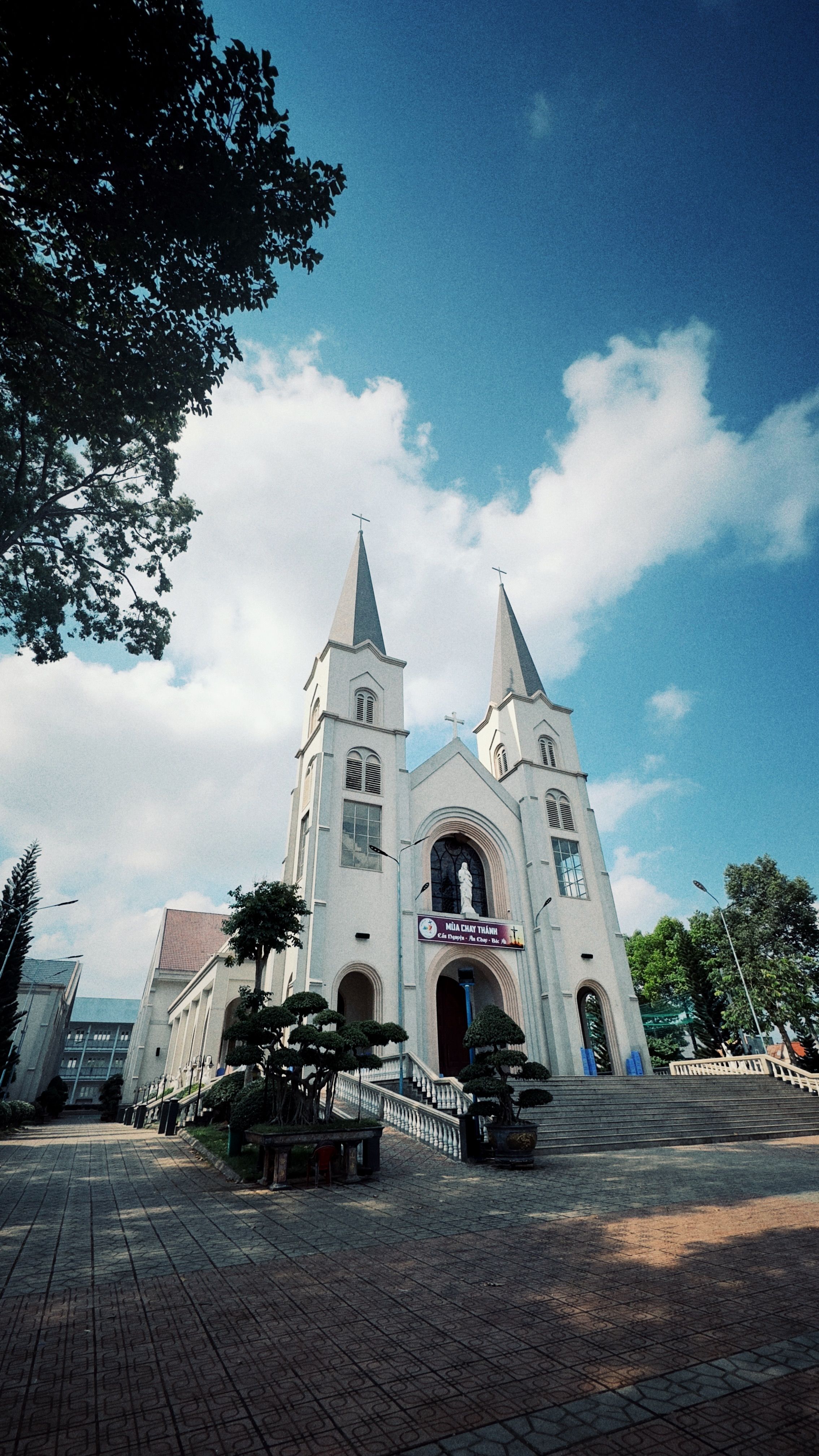 Gothic-style church with two spires framed by trees and blue sky.