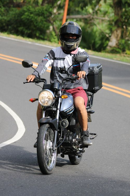 Free A motorcyclist on a sunny day riding down a curved road with greenery. Stock Photo