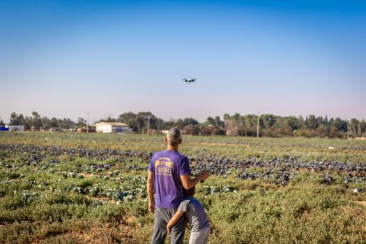 Man and child fly drone over green farmland, capturing scenic rural landscape.