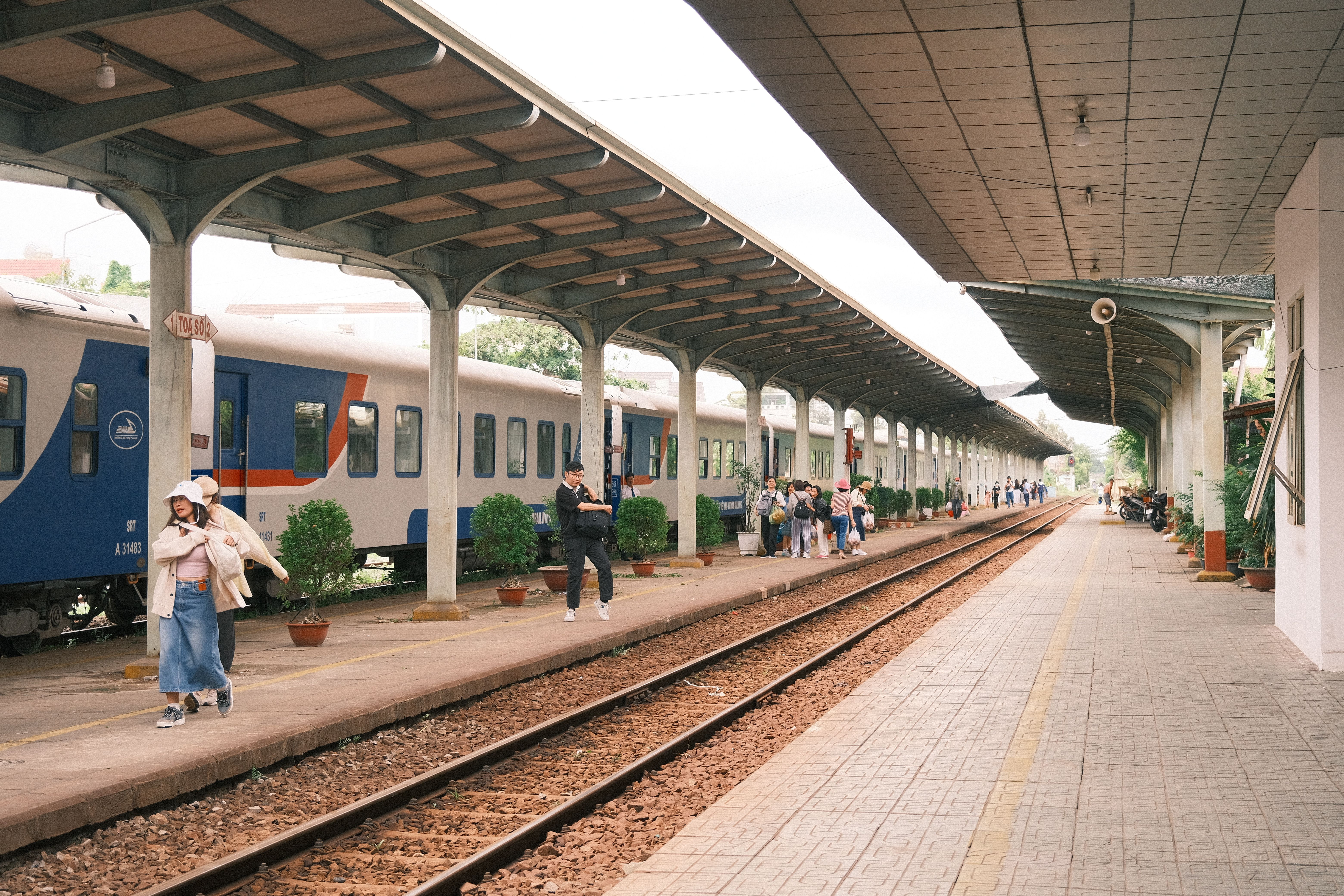 Passengers at a bustling train station platform on a cloudy day.