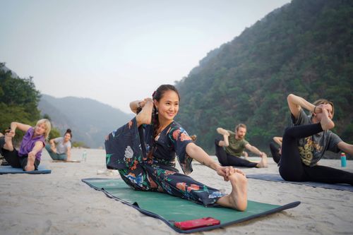 Free Group practicing yoga on a serene beach in Bali, Indonesia, surrounded by lush hills. Stock Photo