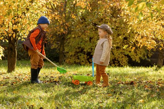 Two children playfully engaging with garden tools in a vibrant autumn setting.