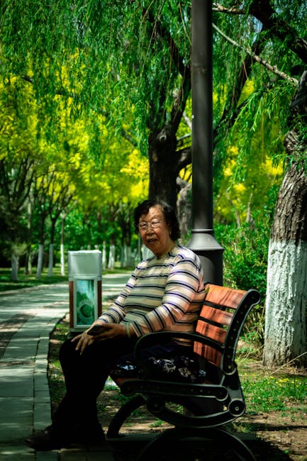 An elderly woman sits on a bench in a lush park in China, enjoying a sunny day.