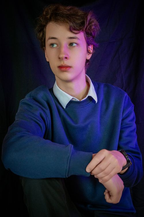 Free A young man in a blue sweater sits pensively with a dark backdrop. Stock Photo