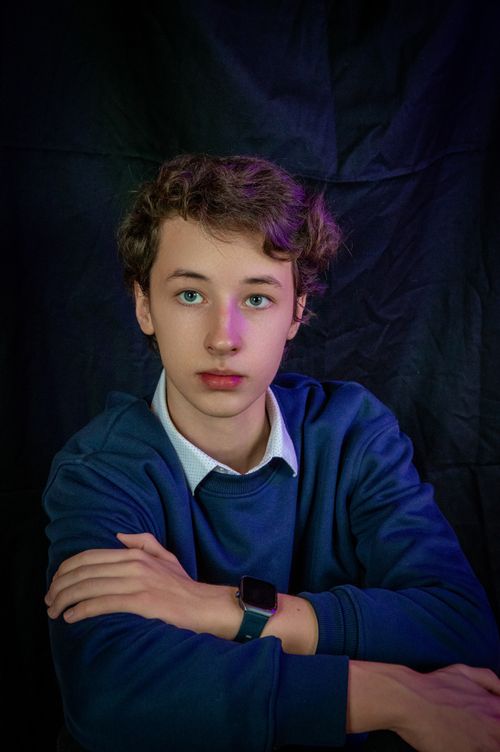 Free Teenage boy poses in casual attire in a studio setting with a dark background. Stock Photo