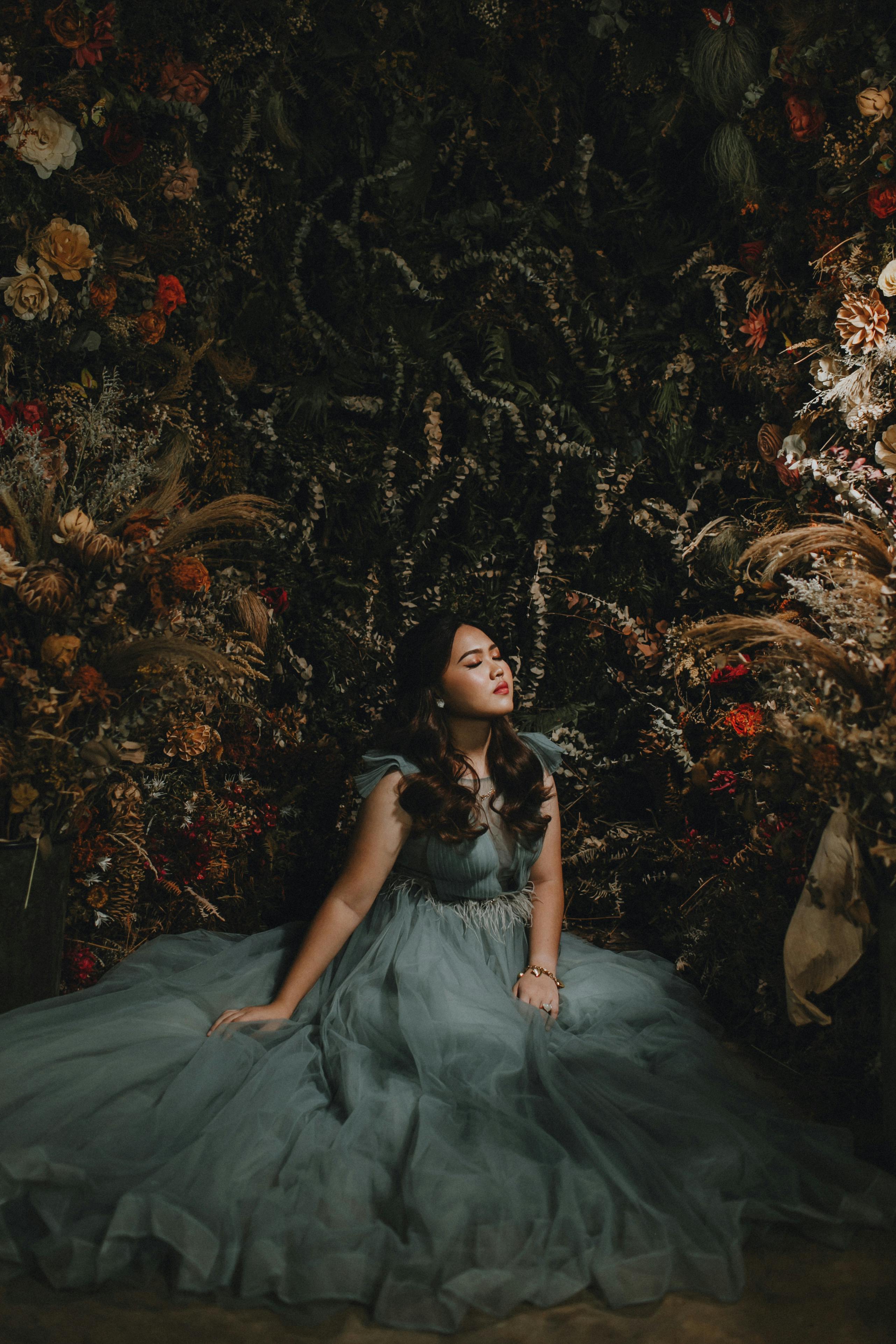 Dreamy portrait of a young woman in a flowing gown surrounded by flowers, showcasing elegance and grace.