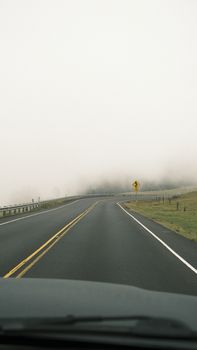 A foggy highway curve disappearing into mist with an empty road ahead.