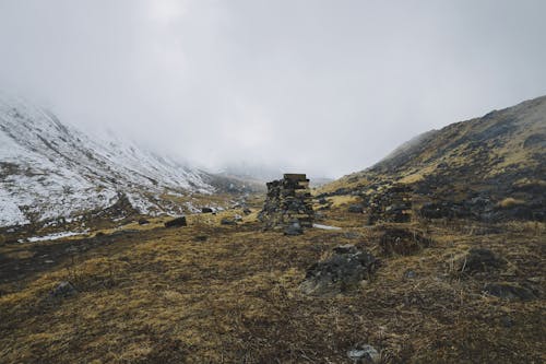 密な雲のある雪をかぶった山の横の枯れた地面にある岩の山のローアングルショット