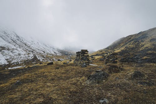 Low Angle Shot Von Steinhaufen Auf Verwelkten Böden Neben Einem Schneebedeckten Berg Mit Dichten Wolken