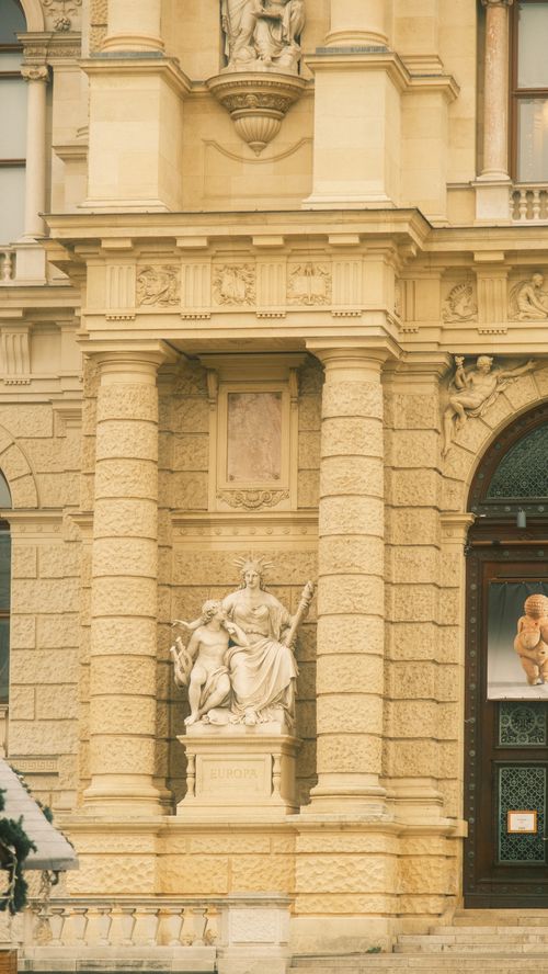 Free Elegant stone sculpture in front of a historic European building facade. Stock Photo