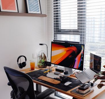 Stylish home office with dual screens, laptop, and tech gadgets by a bright window for optimal productivity.
