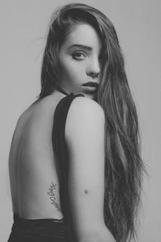 一幅引人注目的黑白肖像中，一位长发女子纹身明显，摆出优雅的姿势