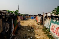 一条尘土飞扬的乡村小路两侧，搭着覆盖防水布和标志的临时避难所