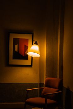 A cozy interior corner with an armchair under warm lamp light beside abstract artwork.