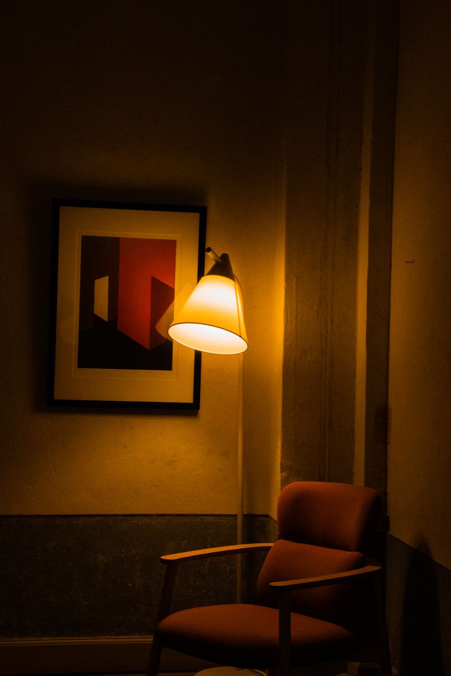 Armchair under a warm wall lamp beside framed art, photo by Nazli Isguven on Pexels