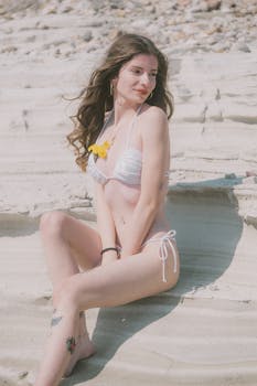 Sun-kissed woman in bikini relaxing on a sandy beach, exuding a boho summer vibe.