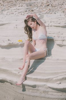 Tranquil beach moment with a woman in white swimwear soaking up the sun on coastal rocks.