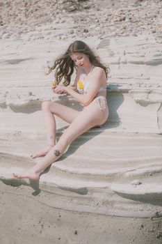 Young woman in boho swimwear relaxing on coastal rocks. Perfect summer vibes.