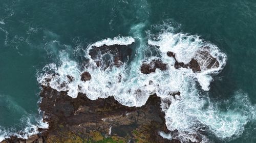 Free Aerial photograph capturing ocean waves crashing onto jagged rocks beneath, showcasing the power of nature. Stock Photo
