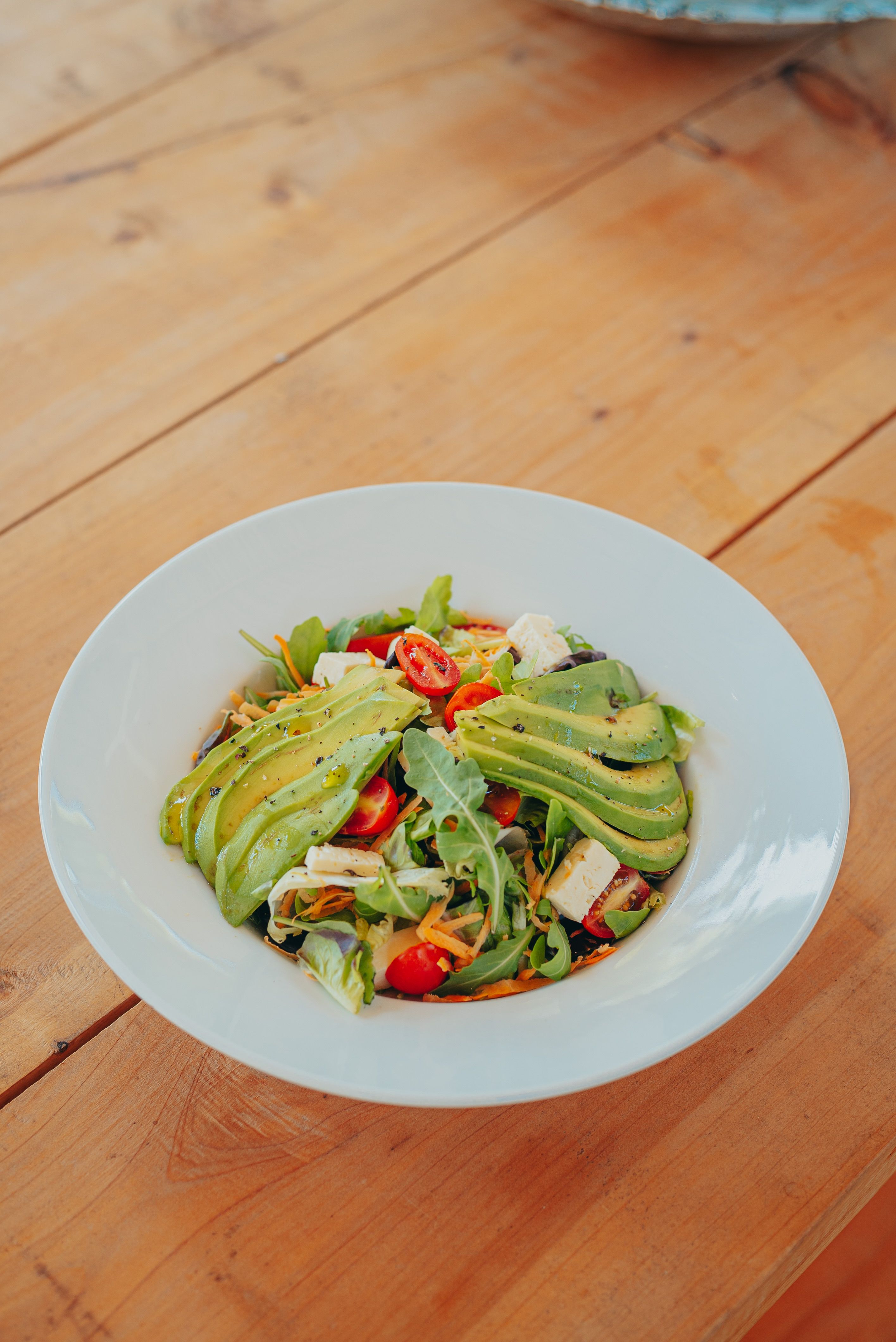 Delicious salad with avocado, arugula, and tomatoes served on a wooden table.