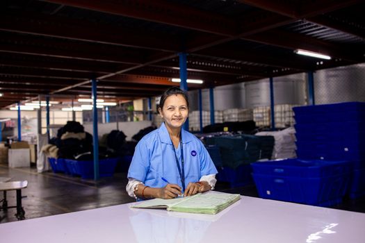 A woman in uniform writing in a notebook inside a textile warehouse.