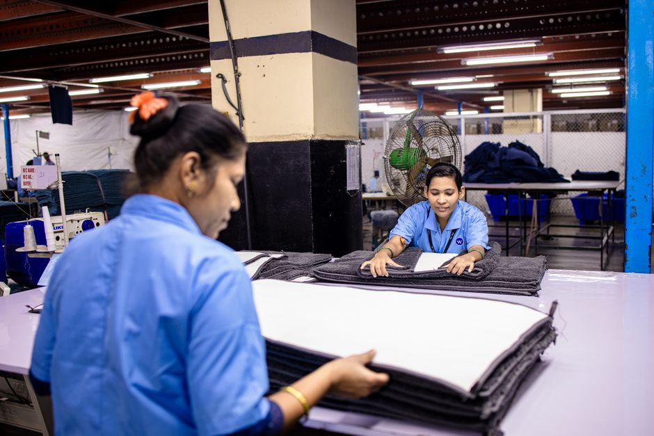 Two workers in a textile factory focus on folding fabric at a well-lit workbench.