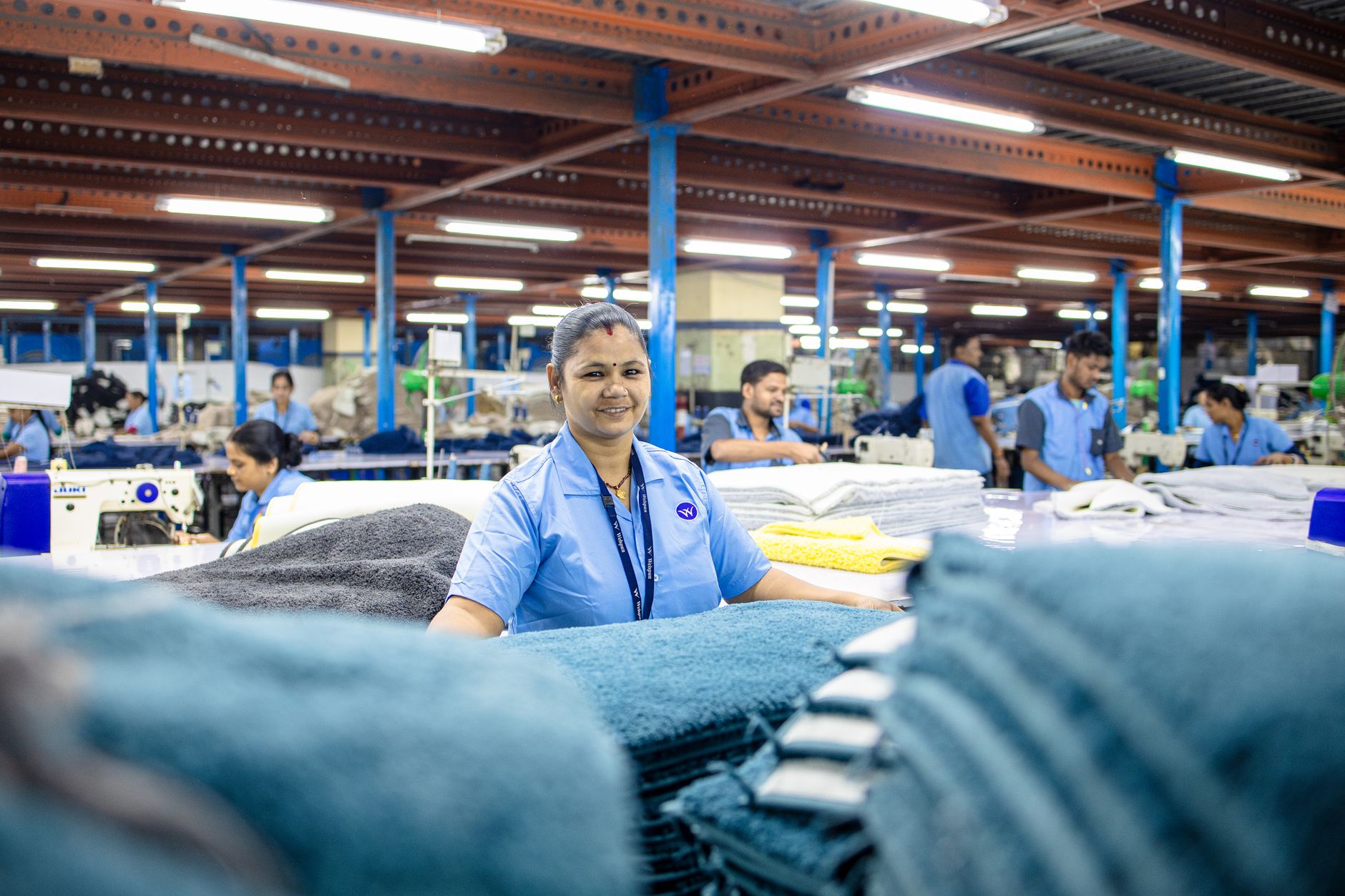A cheerful woman working in a textile factory surrounded by cloth bundles.
