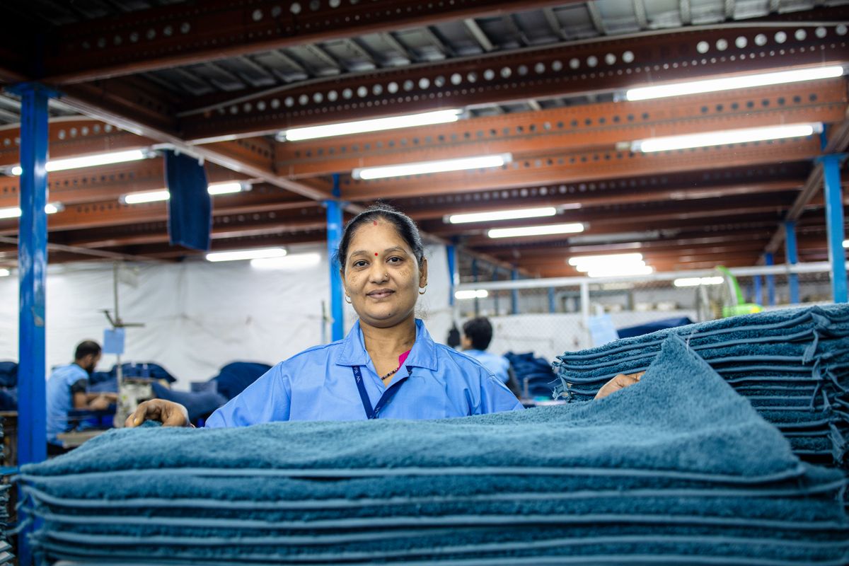 Smiling female textile worker standing in a factory with fabric stacks