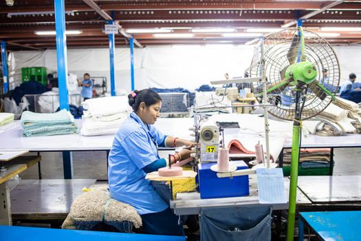 Female worker sewing at textile factory indoor setup, highlighting industrial labor.