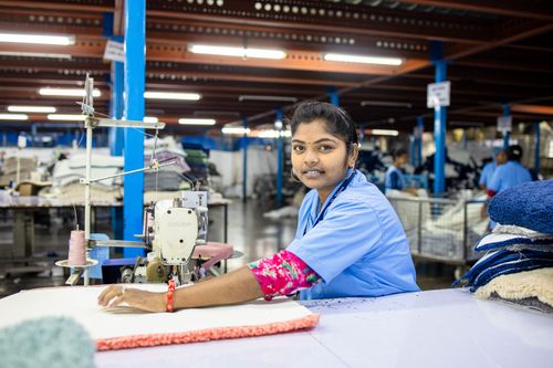 Free Young South Asian female factory worker in blue uniform using sewing machine in textile manufacturing. Stock Photo