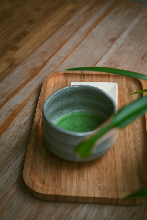 Free Ceramic teacup with vibrant green matcha tea on a rustic wooden tray, creating a serene setting. Stock Photo