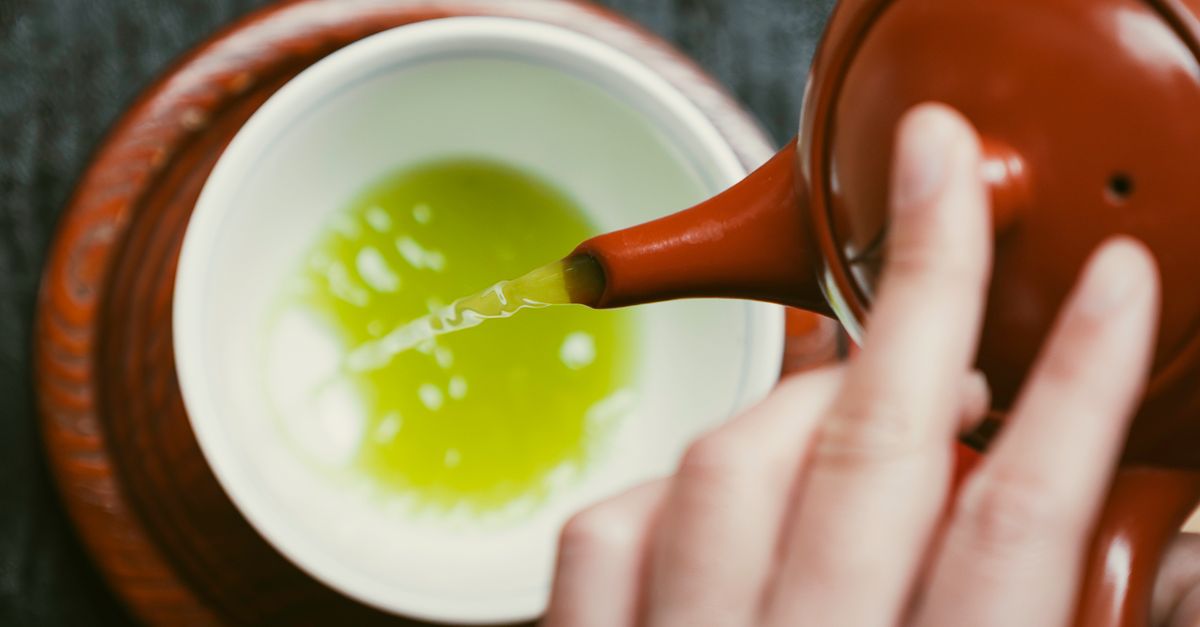 Close-up of green tea being poured from a red teapot into a ceramic cup. - Evidence evidence guide for green tea intake timing glucose lipid metabolism randomized trial