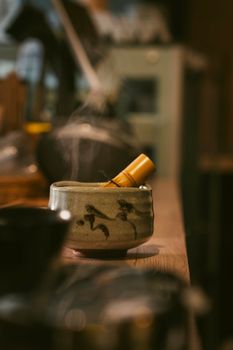Close-up of traditional matcha tea preparation with steam rising from a ceramic bowl. Shot indoors.