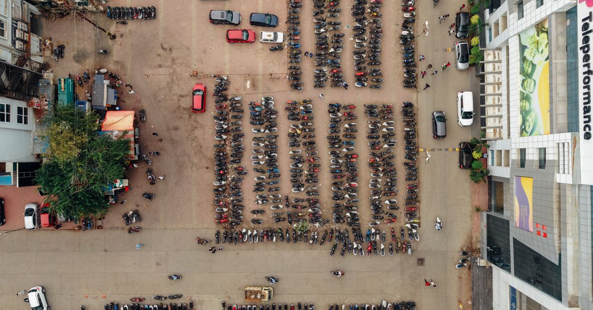Drone shot capturing parked motorcycles and cars in a busy urban parking lot.