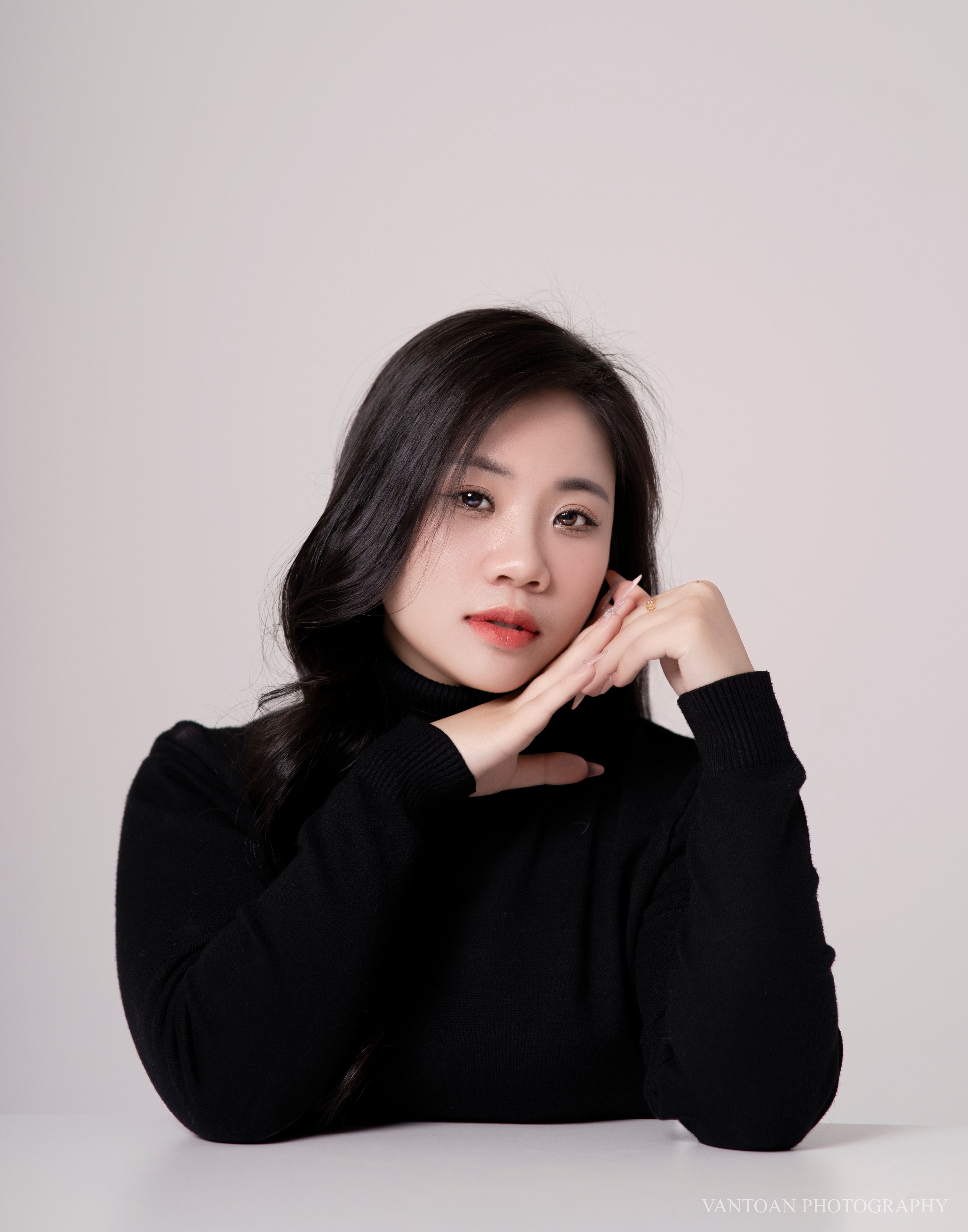 Studio portrait of a thoughtful woman in a black turtleneck against a neutral background.