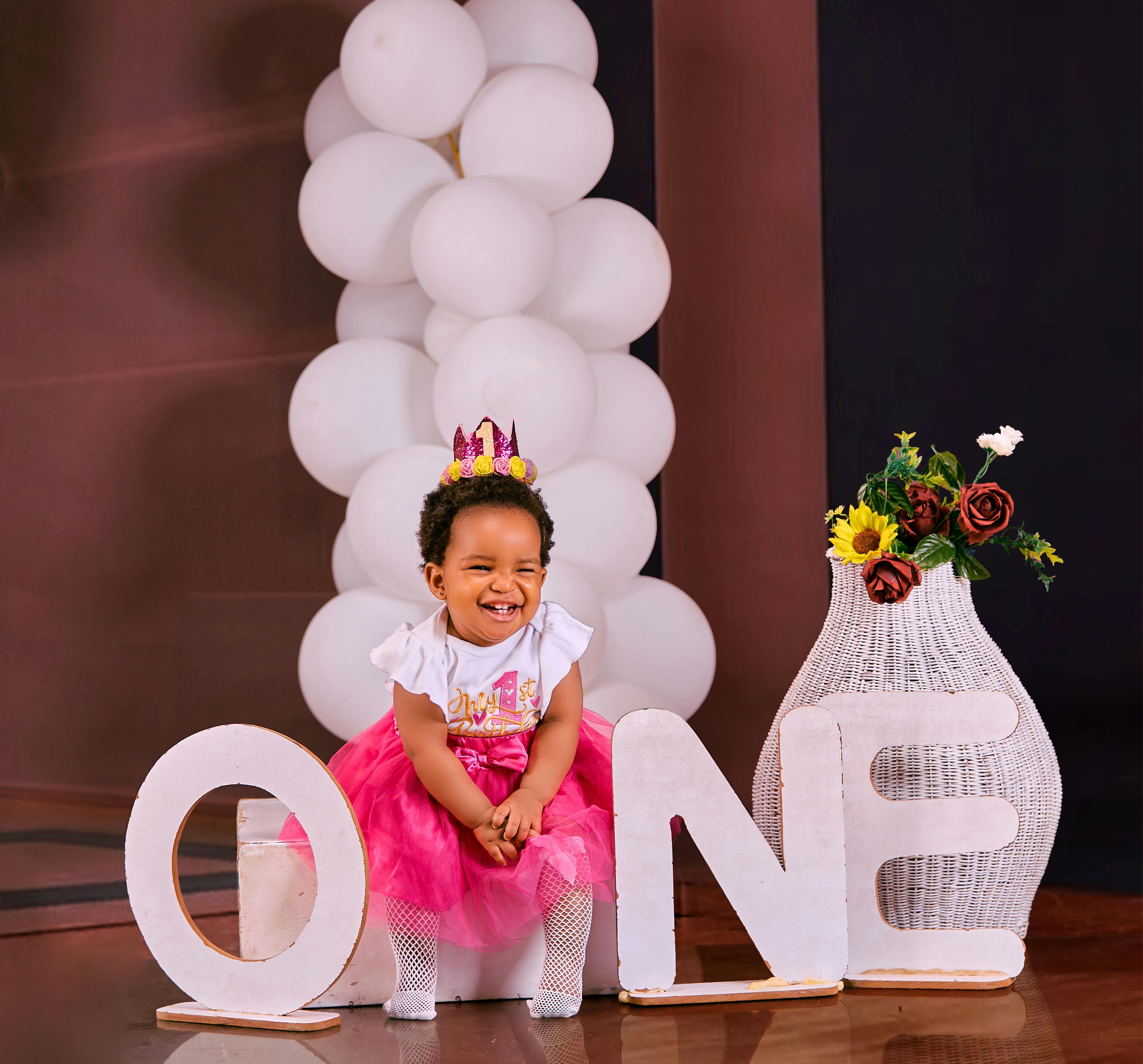 Adorable baby in pink tutu celebrating first birthday with balloons and flowers.