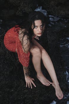 Beautiful woman in red dress sitting on rocky shore in Antalya, Türkiye.