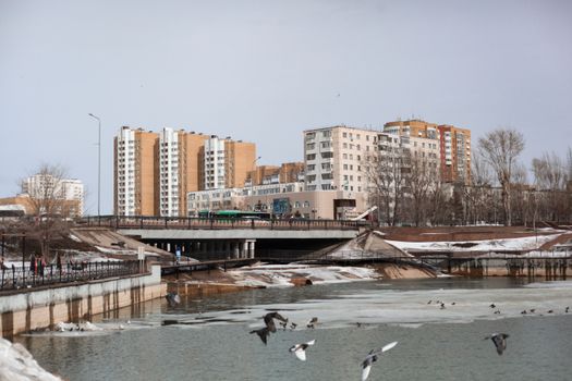 Astana cityscape showcasing riverside buildings and urban architecture under a cloudy sky.