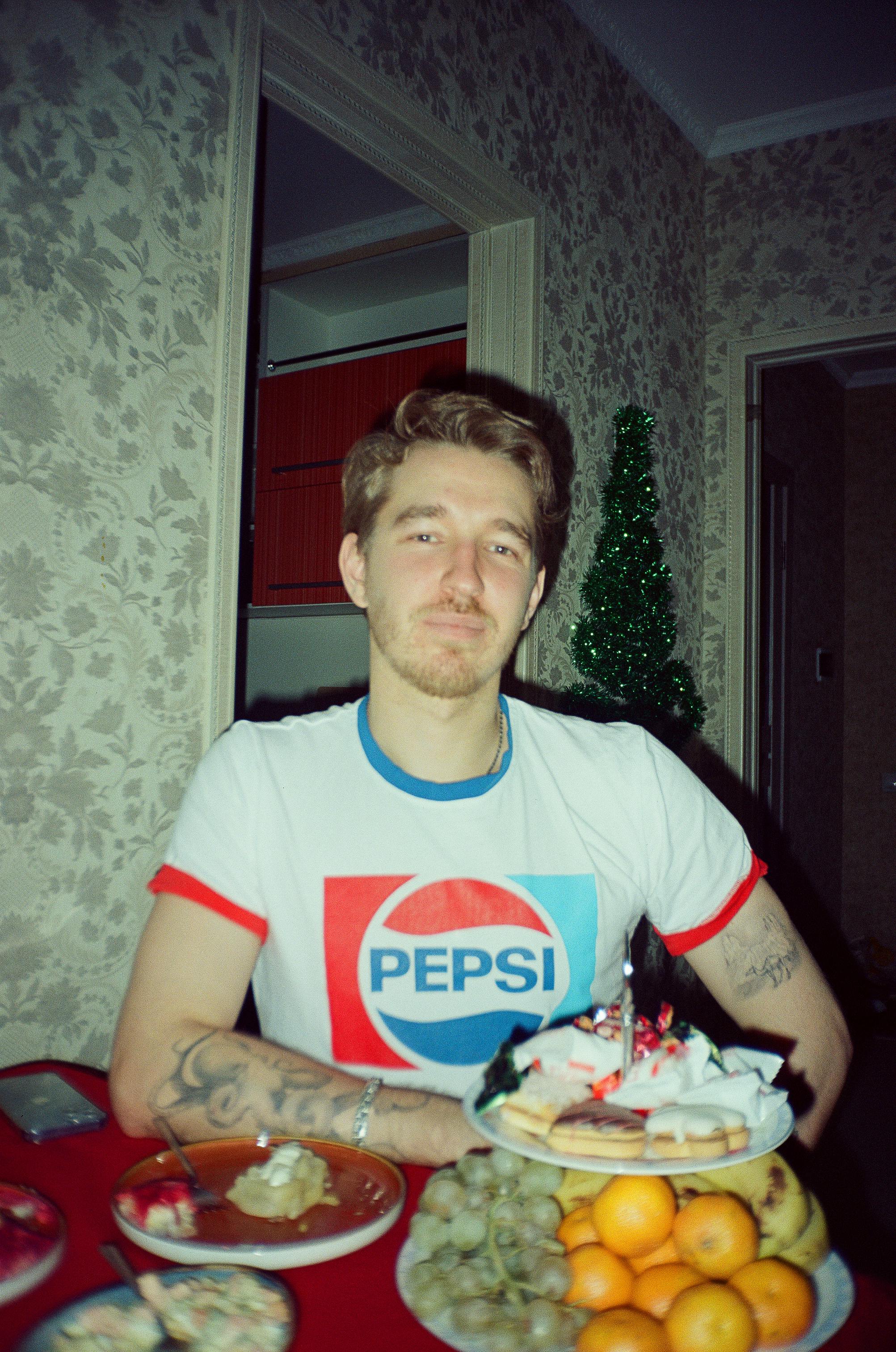A man with tattoos enjoys a festive meal indoors, featuring fruits and a decorated setting.