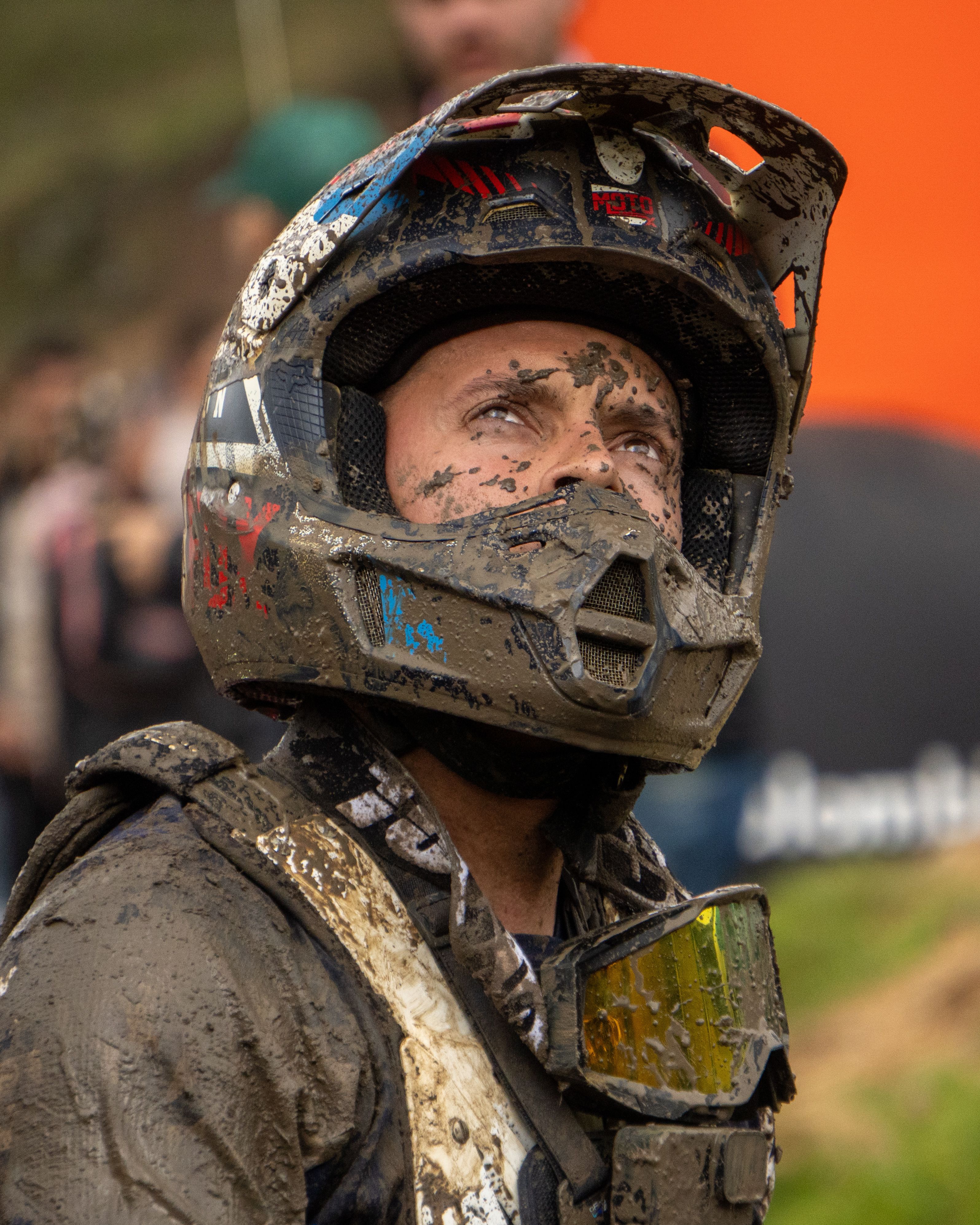 A mud-covered motocross rider looks up with determination during a challenging outdoor event.